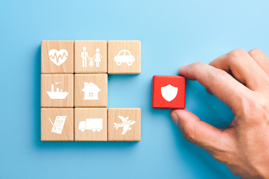 Hand placing a red insurance block among wooden blocks with coverage icons
